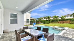 An outdoor patio with a pool, wicker furniture, and a view of a residential area. - Modern Home near Disney: Private Pool, Ping Pong & Waterpark - 7758WL (Kissimmee)