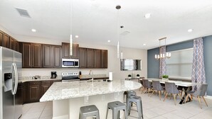 A modern kitchen with granite countertops, stainless steel appliances, and a central island with bar stools. - Modern Home near Disney: Private Pool, Ping Pong & Waterpark - 7758WL (Kissimmee)
