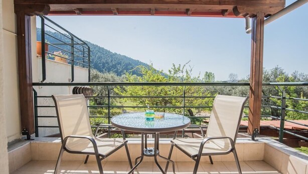 Een balkon met een ronde tafel en twee stoelen, met uitzicht op een bergachtig landschap.