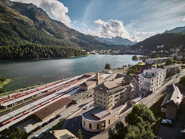 A train station with multiple tracks, a round building, and a lake with mountains in the background.
