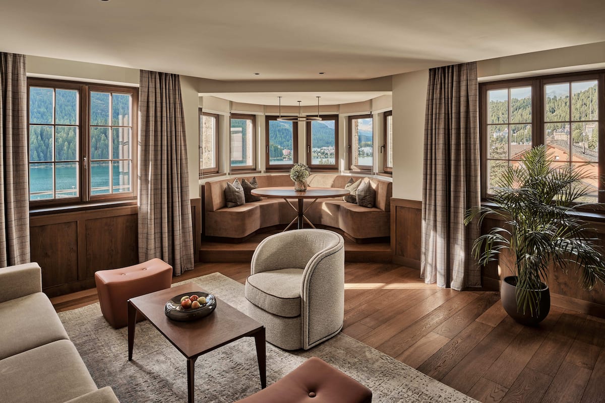 A cozy room with a round table, seating, and large windows overlooking a lake.