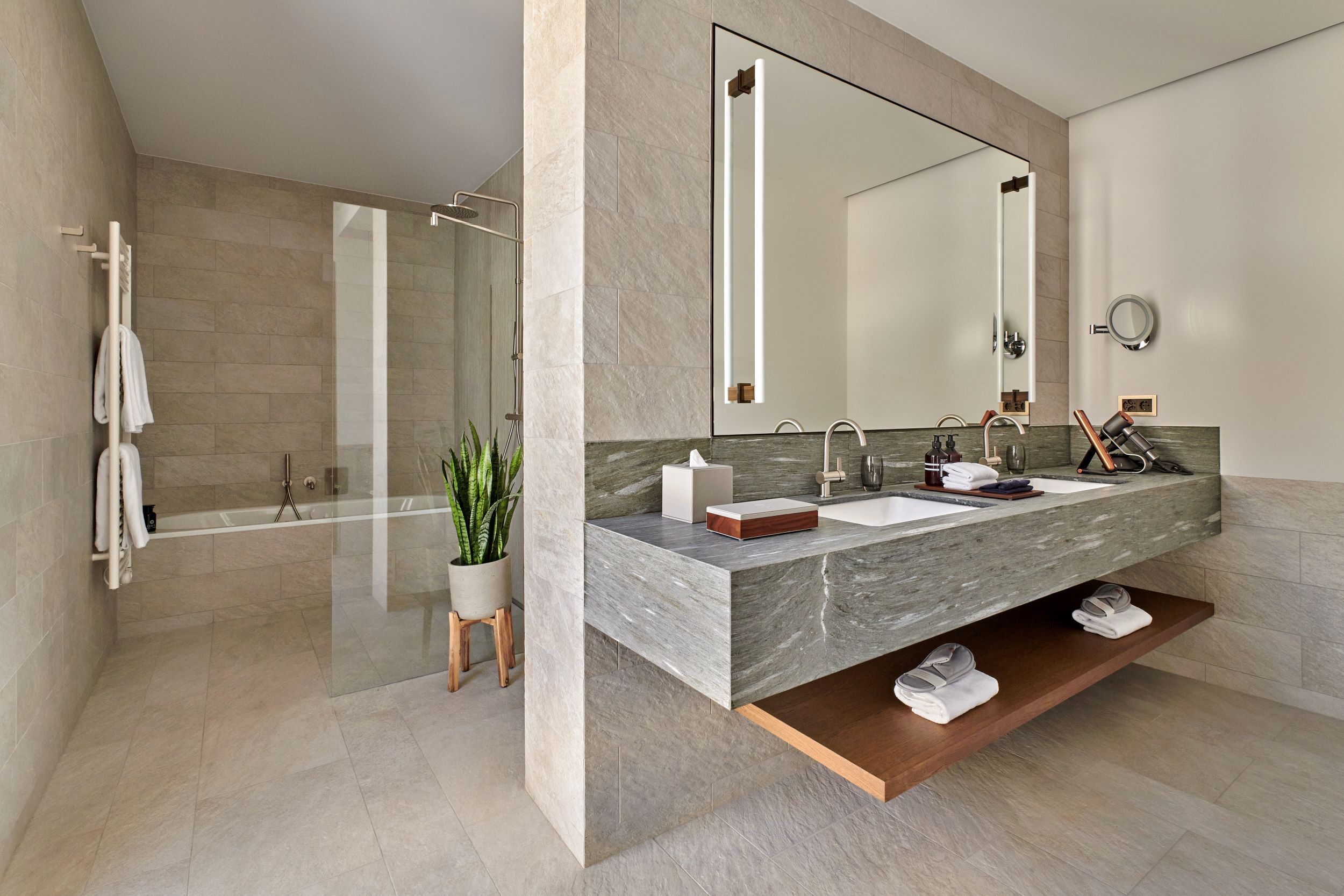 A modern bathroom with a large mirror, dual sinks, and a shower area.