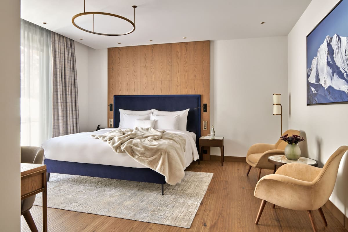 A modern hotel room with a large bed, wooden headboard, a desk, and a chair.