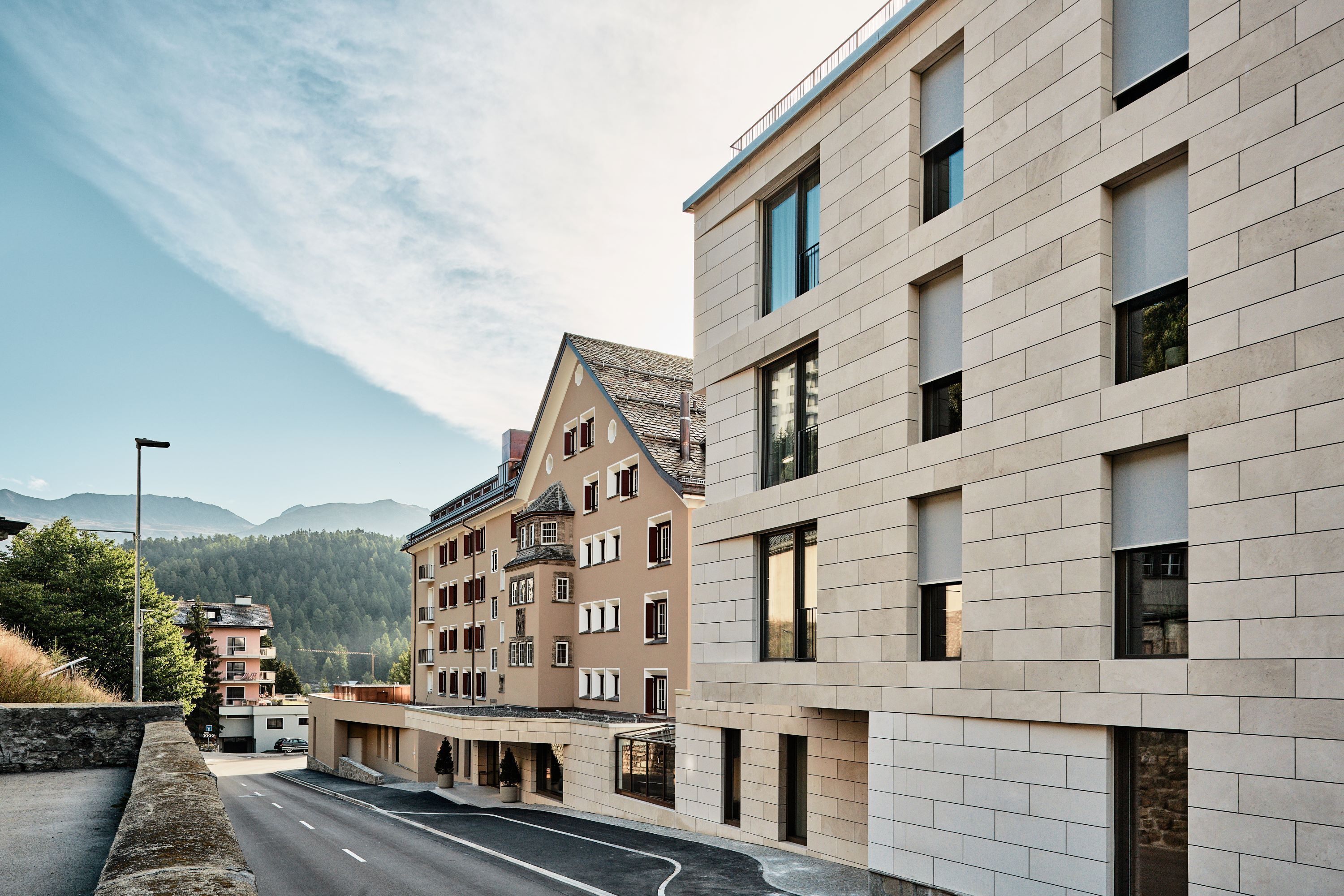 A modern hotel with a flat roof, large windows, and a view of mountains.