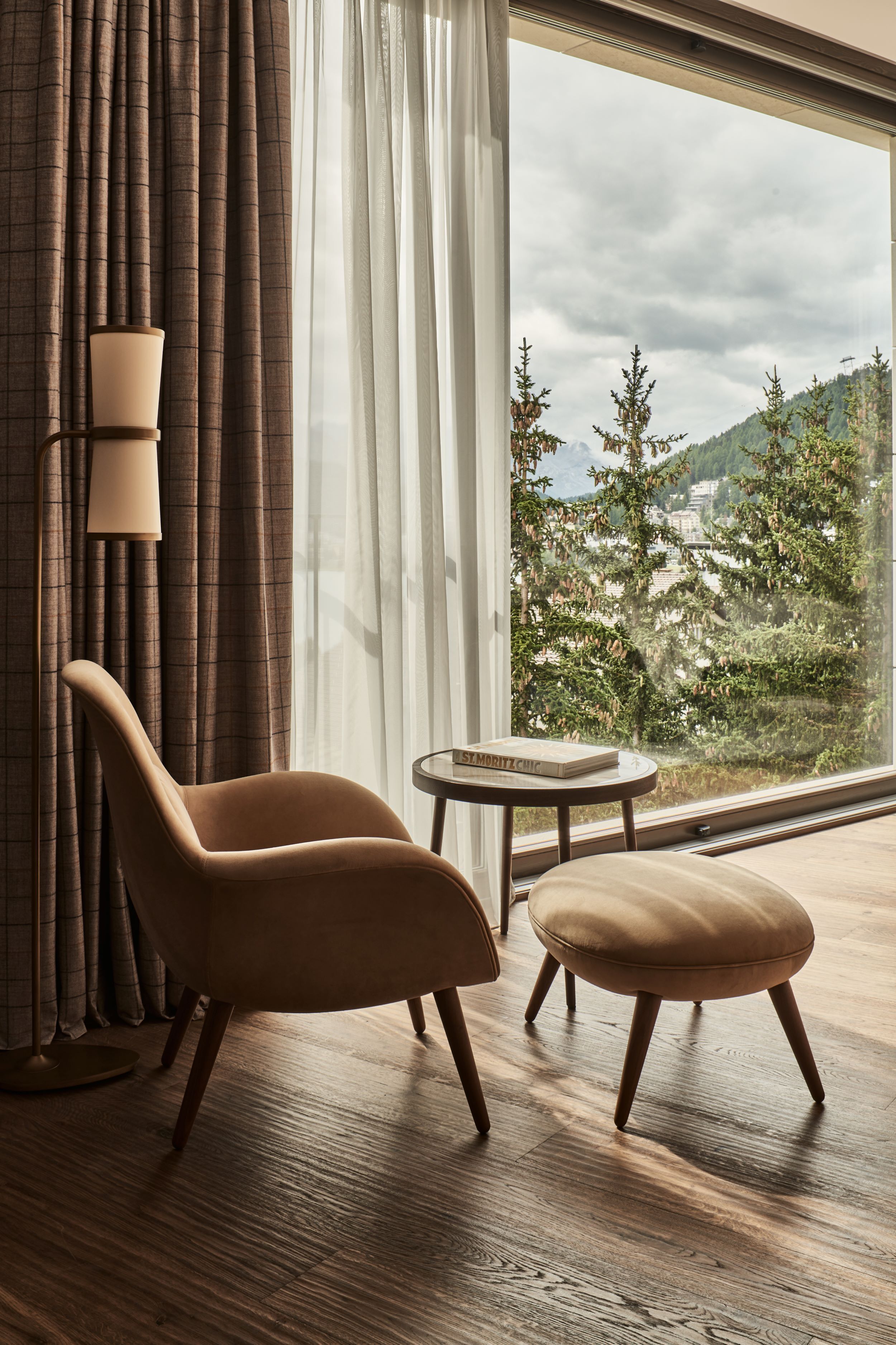 A room with a large window, a brown chair, a small table, and a lamp.
