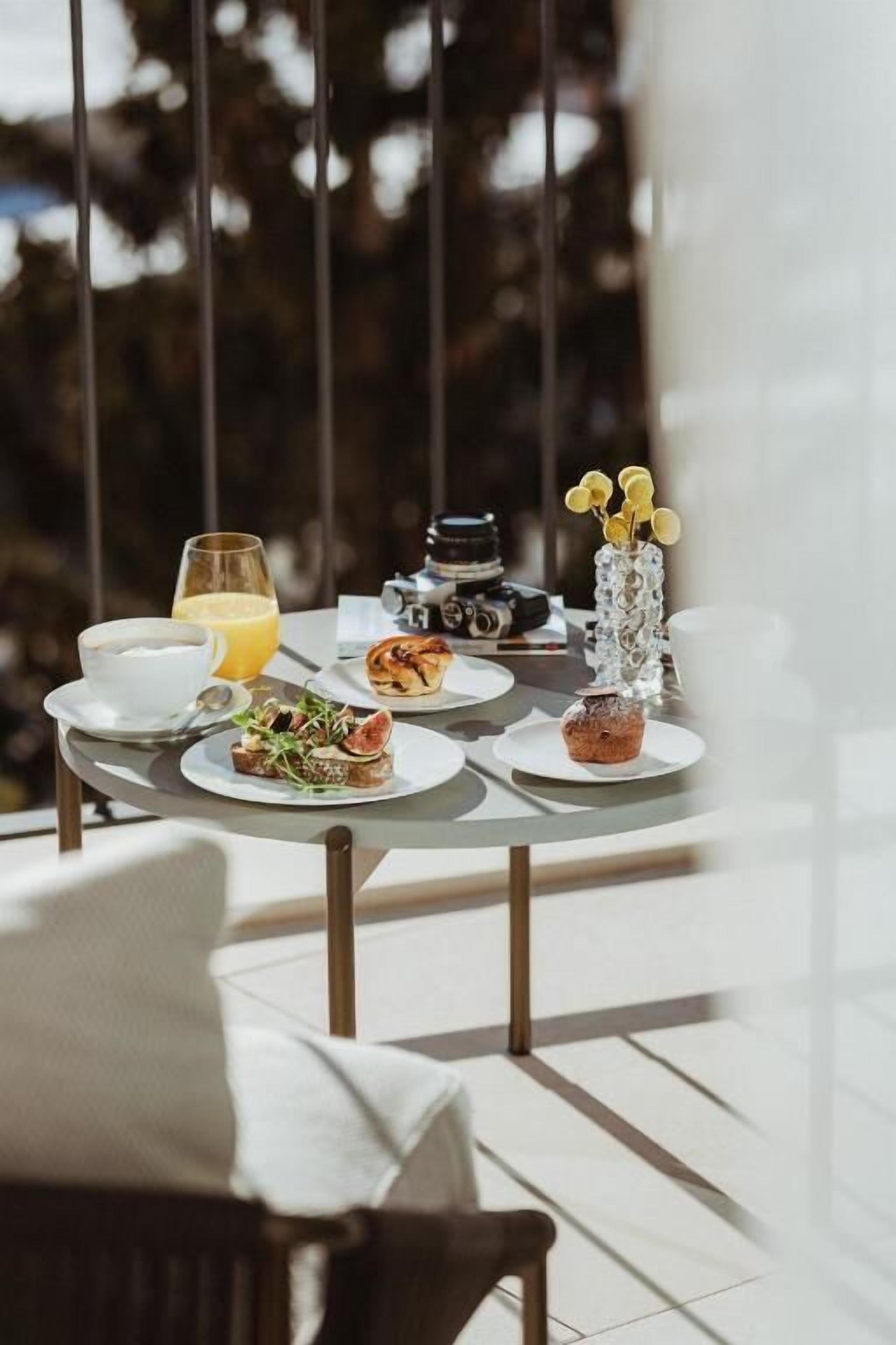 Une table à manger avec des assiettes remplies de nourriture, un verre de jus d’orange et un appareil photo sur le balcon.