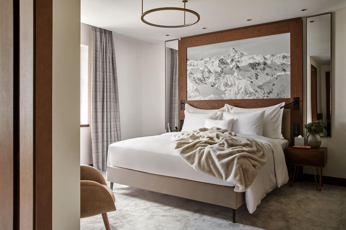 A modern bedroom with a large bed, a wooden headboard, a bedside table with a vase, and a large mirror.
