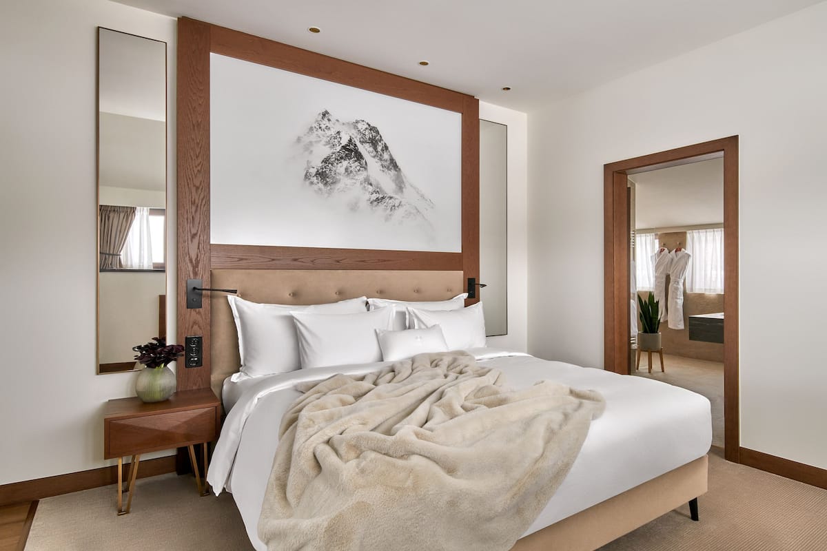 A modern bedroom with a large bed, a wooden headboard, a large mirror, and a wall-mounted artwork.