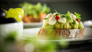 Un sandwich garni d’avocat, de fromage et de légumes verts, servi sur une tranche de pain.
