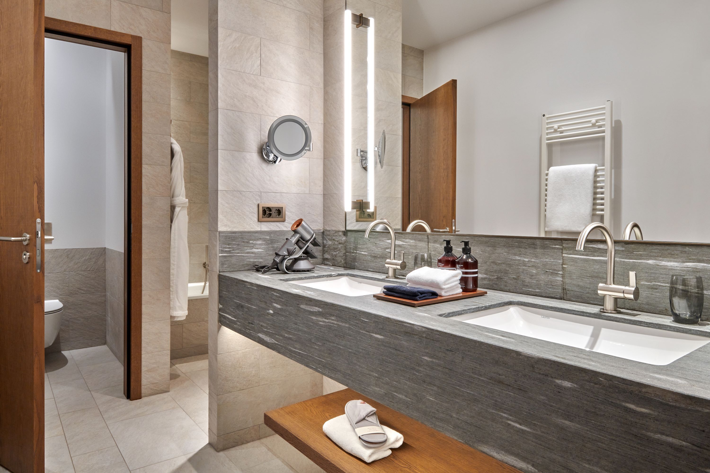 Ein modernes Badezimmer mit zwei Waschbecken, einem großen Spiegel und einer hölzernen Sitzbank.
