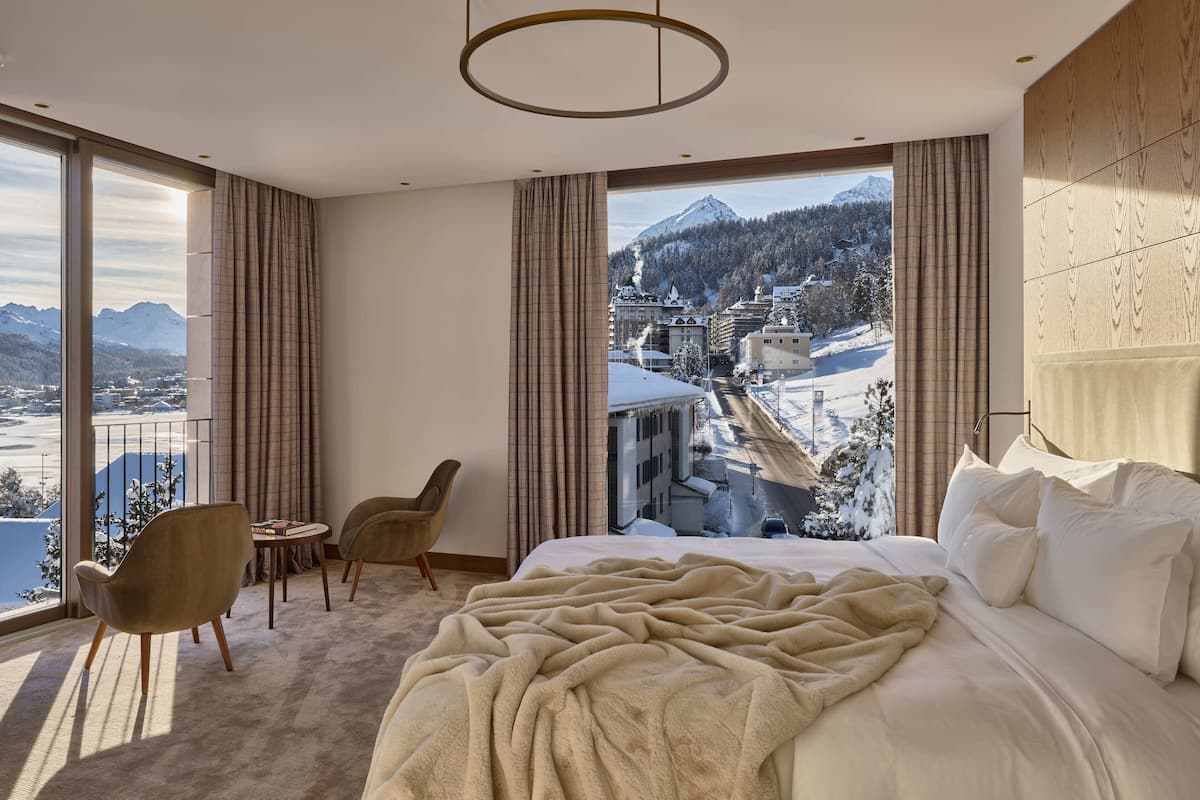 A bedroom with a large bed, a view of a snowy mountain, and a balcony with a chair and table.