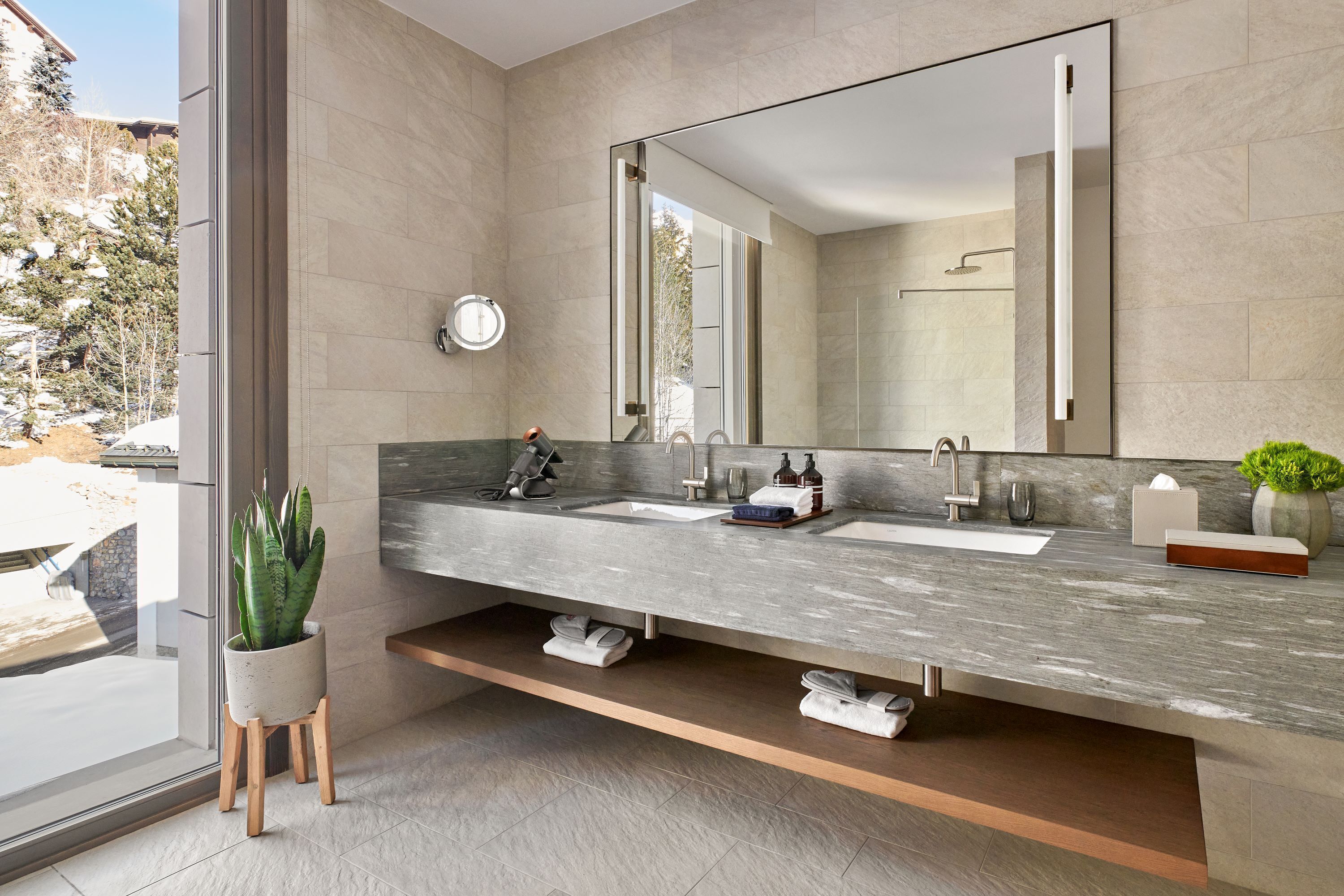 Un baño moderno con un espejo grande, dos lavamanos y una planta en maceta.