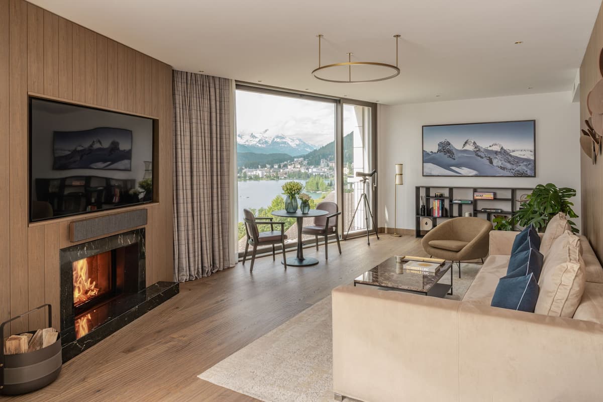 A modern living room with a fireplace, a sofa, a coffee table, and a view of a lake and mountains.