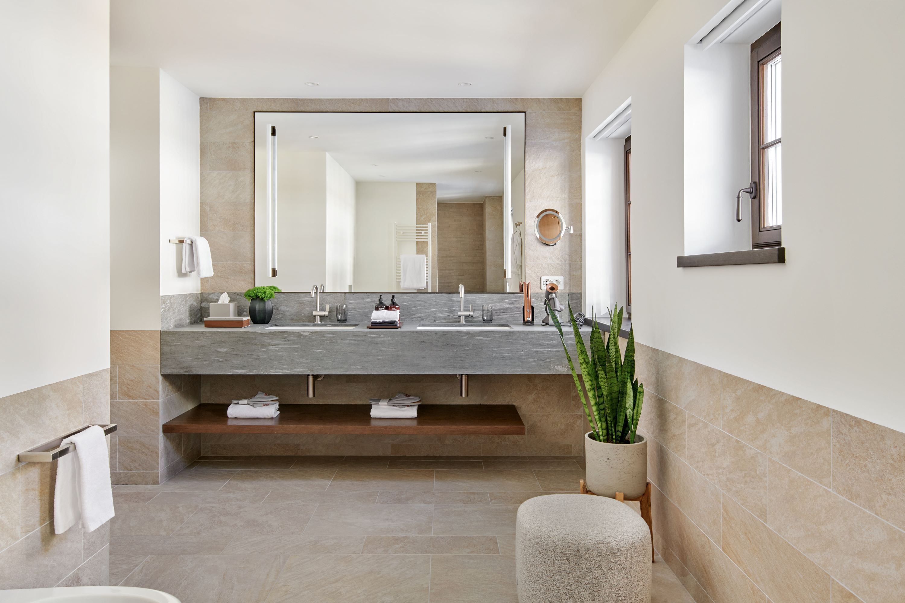 Un baño moderno con un espejo grande, lavamanos dobles y un estante empotrado.