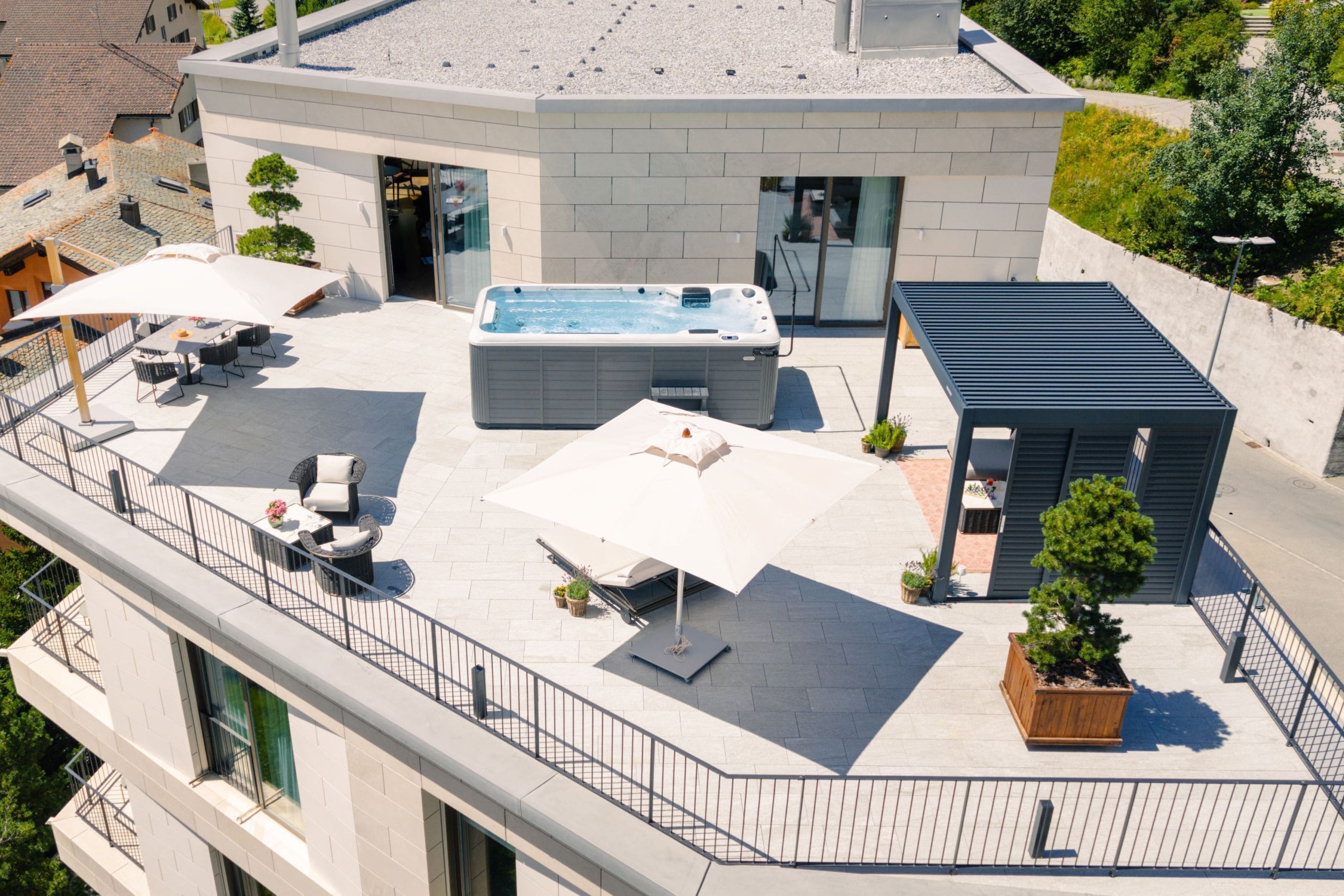A rooftop with a hot tub, outdoor seating, and a small wooden structure.