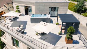 A rooftop with a hot tub, outdoor seating, and a small wooden structure.