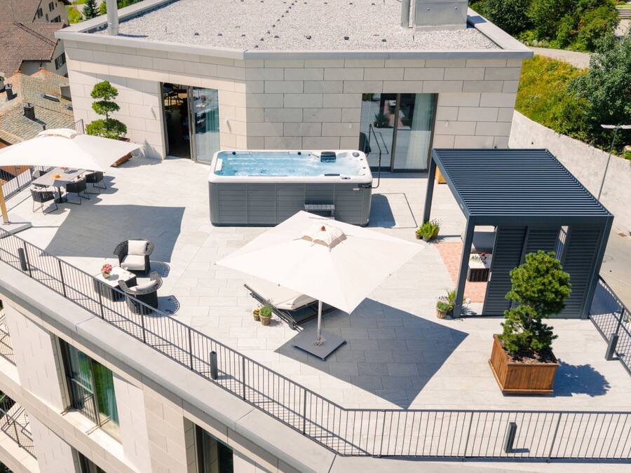 Una terraza con jacuzzi, mobiliario exterior y una pequeña estructura de madera.