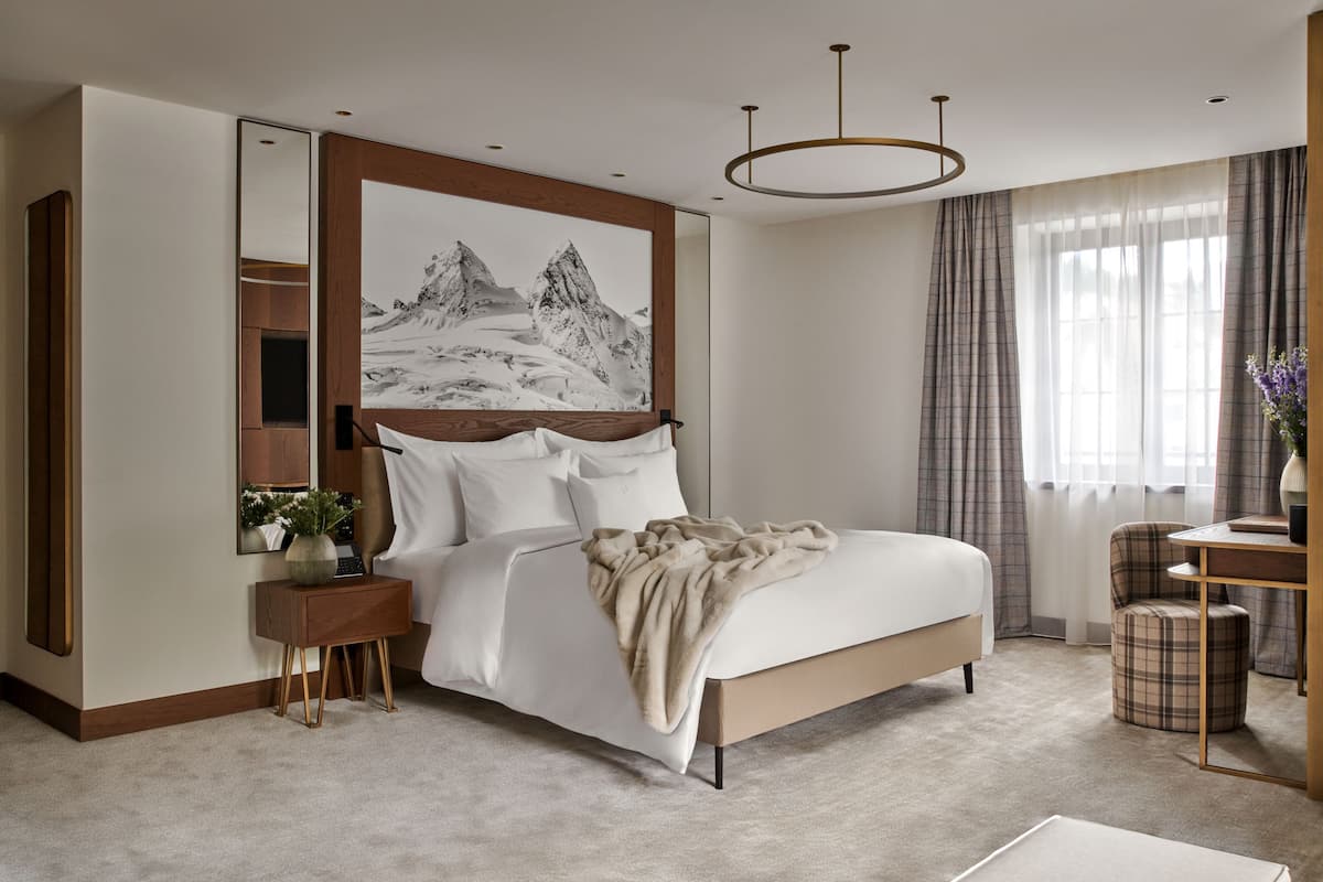 A bedroom with a large bed, a bedside table with a vase, a mirror, and a painting of mountains.