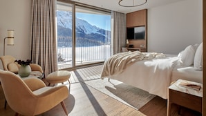 A modern hotel room with a large bed, a sofa, a TV, and a view of snow-capped mountains. - Hotel GRACE LA MARGNA ST MORITZ (St. Moritz)