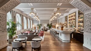 A spacious bar area with high ceilings, ornate moldings, and a variety of seating options including round tables and bar stools. - Hotel GRACE LA MARGNA ST MORITZ (St. Moritz)
