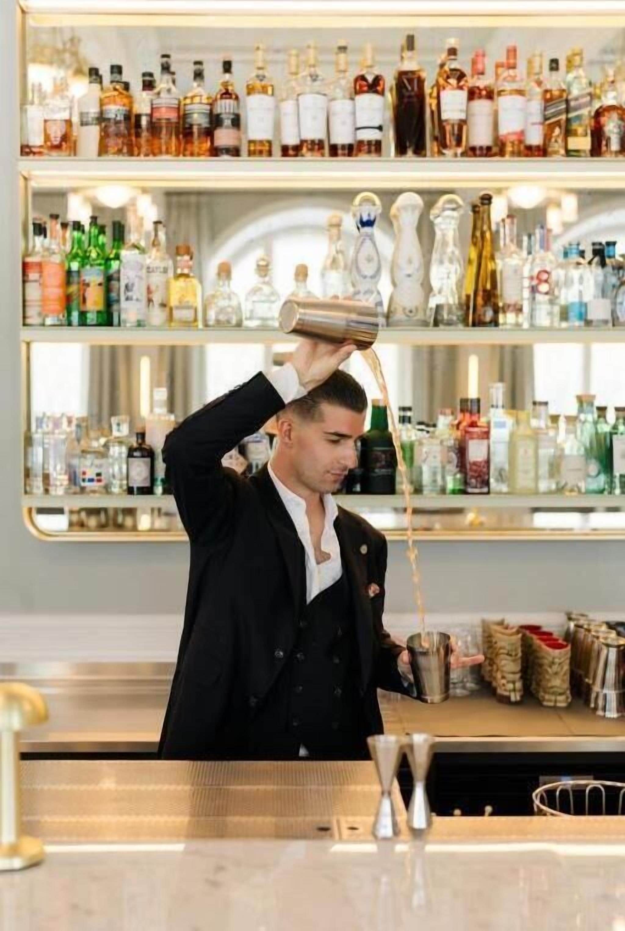 Un bartender vertiendo una bebida en una coctelera.