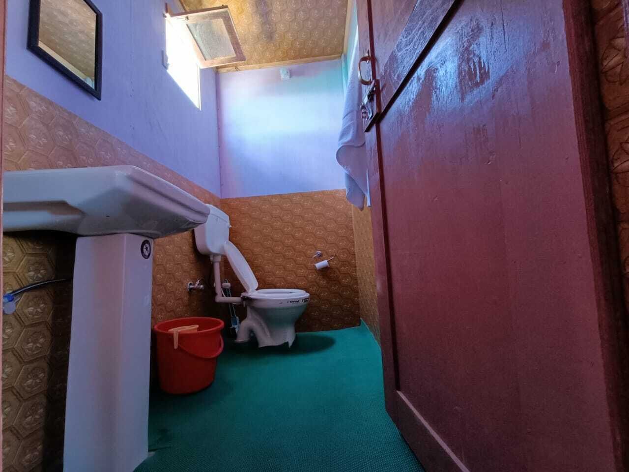 Ein kleines Badezimmer mit Toilette, einem roten Eimer und einem grünen Boden.