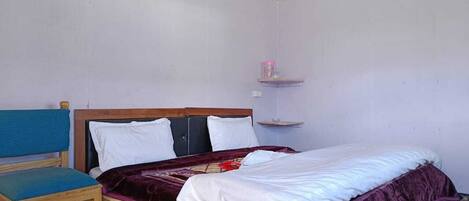 A single bed with a wooden headboard, a blue upholstered chair, and a small shelf with a pink object.