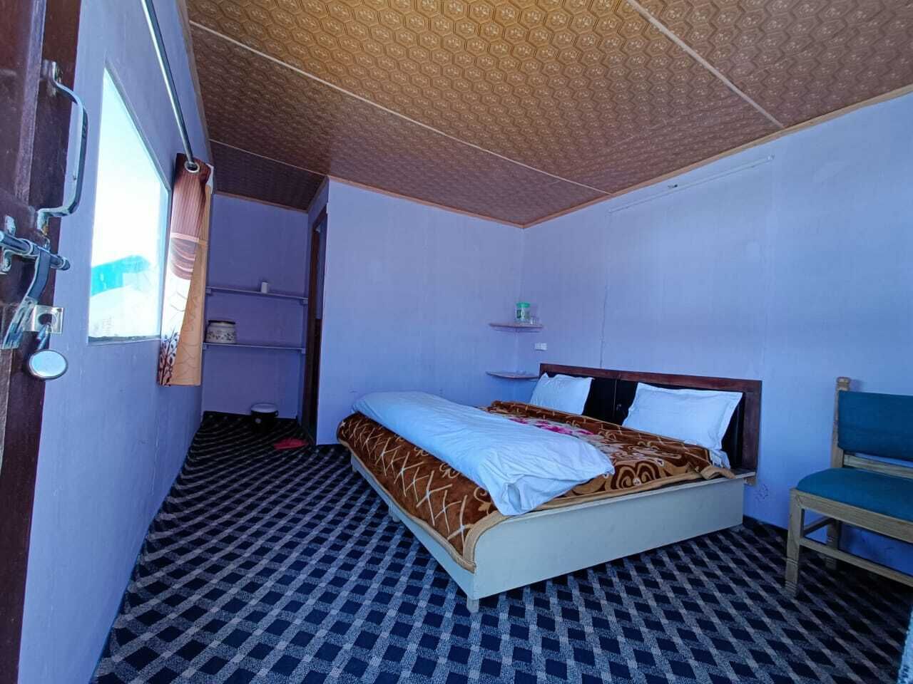 A small, single-bed room with a checkered floor, a wooden ceiling, and a simple bed with a headboard.