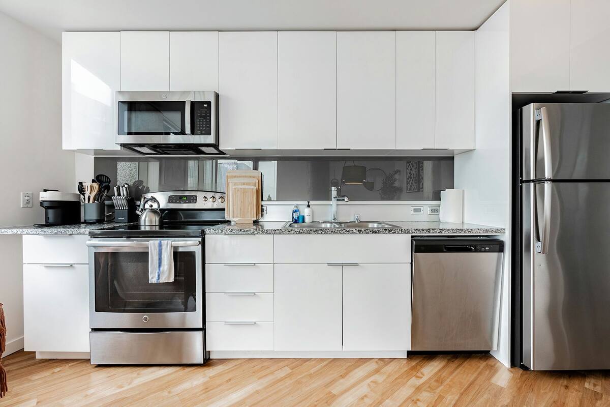 A modern kitchen with white cabinets, stainless steel appliances, a microwave, oven, dishwasher, and a refrigerator.