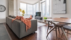 A modern living room with a grey sofa, a dining table, and a TV. - Sophari Towers: Bellevue Apartments  (Bellevue)