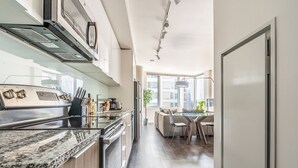 A modern kitchen with a granite countertop, stainless steel appliances, and a dining area with a glass table and chairs. - Sophari Towers: Bellevue Apartments  (Bellevue)