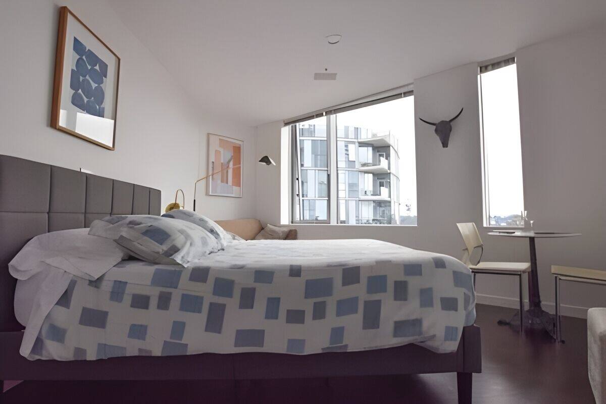 A modern bedroom with a large bed, a desk, and a window with a city view.