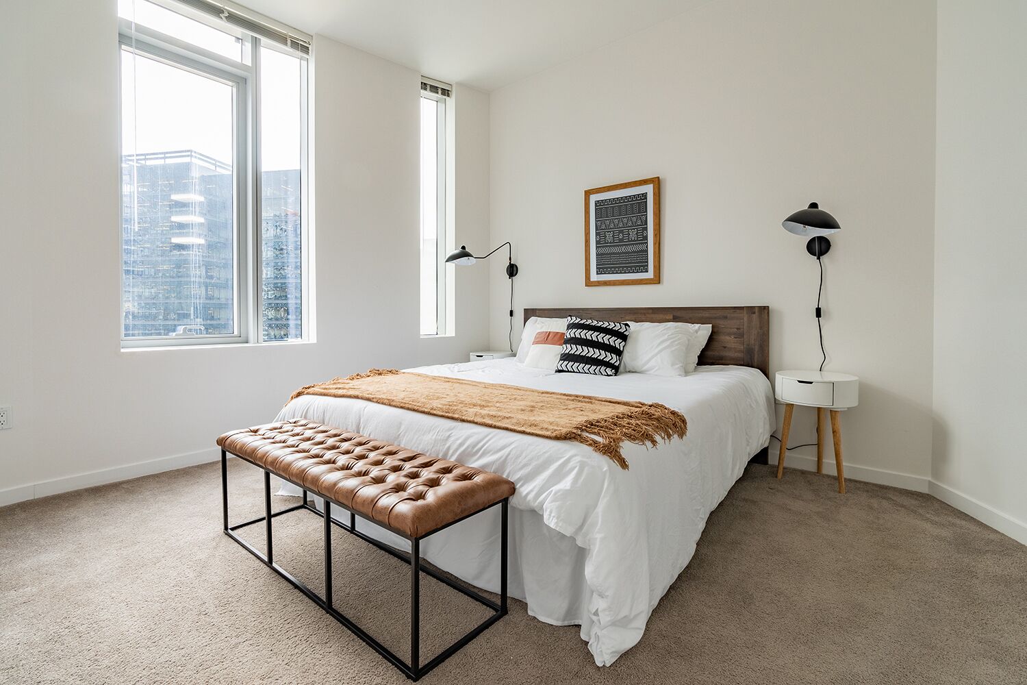 A bedroom with a large bed, a bench, two bedside lamps, and a framed picture on the wall.