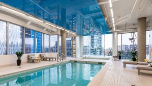 An indoor swimming pool with clear glass walls, lounge chairs, and potted plants. - Sophari Towers: Bellevue Apartments  (Bellevue)
