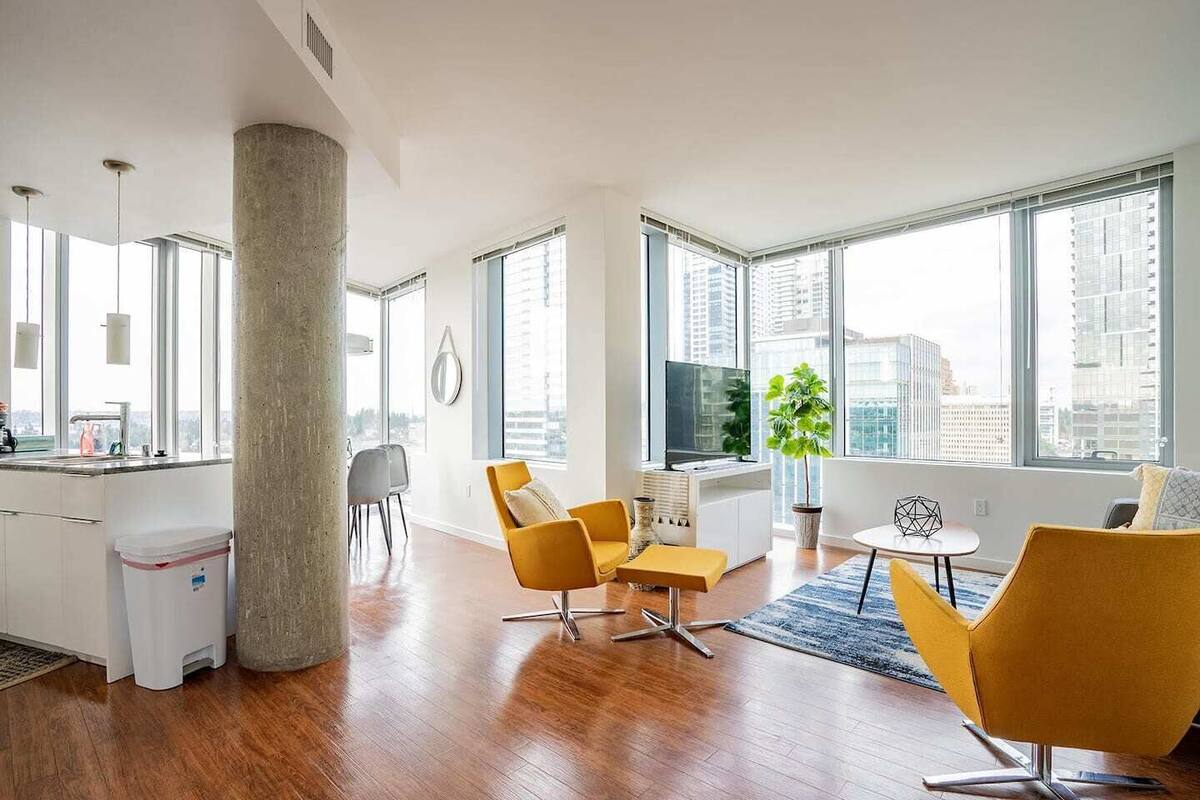 A modern living room with a kitchen area, large windows, and a city view.