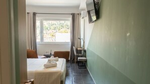 Une chambre d’hôtel comprenant un lit, un bureau, une chaise, un téléviseur fixé au mur et une fenêtre avec des rideaux.