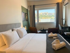 Quarto de hotel com uma cama, duas cadeiras, uma escrivaninha, uma janela com vista para um local histórico e um abajur.