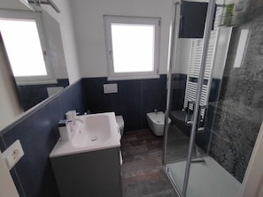 Een moderne badkamer met een douchecabine van glas, een witte wastafel en een toilet.