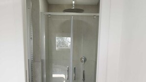 A glass-enclosed shower with a handheld showerhead and a wall-mounted faucet.