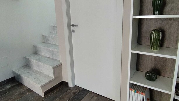 A staircase leading to a door, a shelf with decorative items, and a wall-mounted thermostat.