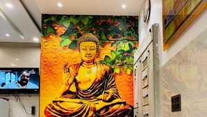 A room with a large Buddha mural, a sofa, and a television. - Hotel 4S Niwas (Amritsar)