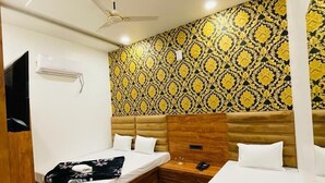 A hotel room with two beds, wooden headboards, a ceiling fan, and a patterned wallpaper. - Hotel 4S Niwas (Amritsar)