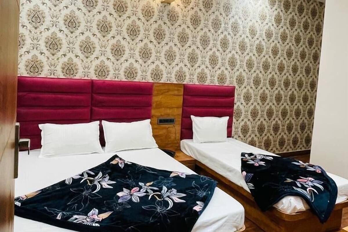 Una habitación de hotel con dos camas, un cabecero rojo, papel tapiz estampado y un ventilador de techo.
