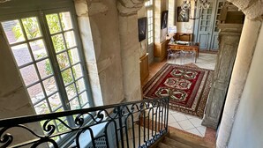 A staircase leading to a dining area with a red patterned rug, a chandelier, and a view of greenery outside. - Côté Park (Givry)