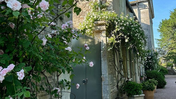 A stone building with a brick chimney, a green door, and a gravel path leading to a gate. - Côté Park (Givry)