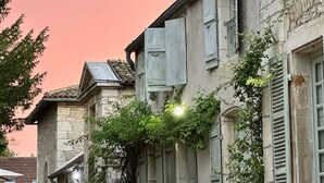 A stone building with a garden in front, featuring a large planter with flowers and a metal sculpture. - Côté Park (Givry)