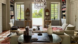 A spacious room with a large chandelier, a sofa, a coffee table, and bookshelves filled with books. - Côté Park (Givry)