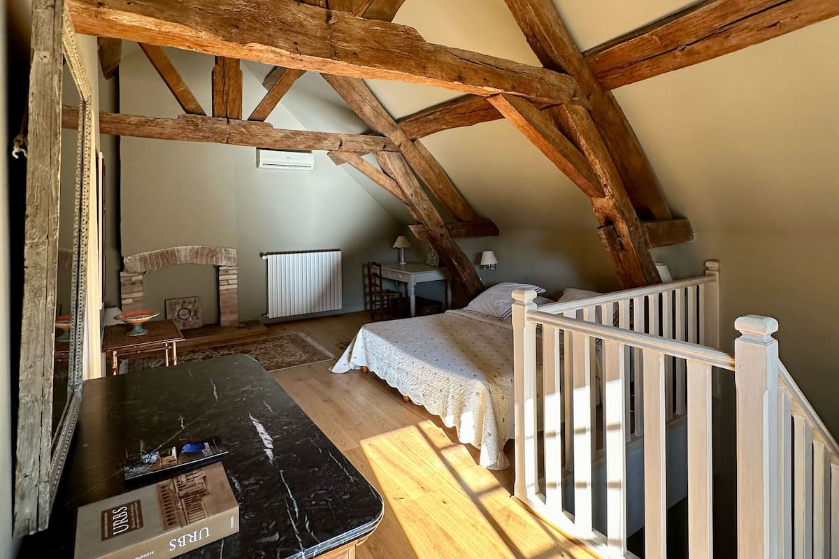 A cozy attic bedroom with exposed wooden beams, a bed, a desk, and a small table.