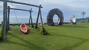 Une zone herbeuse avec une aire de jeux comprenant des balançoires, une grande sculpture circulaire et une structure en forme de cœur.
