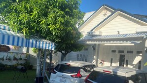Deux VUS Mitsubishi blancs sont stationnés dans une allée menant à une maison dotée d’une terrasse carrelée, d’un espace extérieur aménagé avec des meubles de jardin et d’une porte de garage blanche.